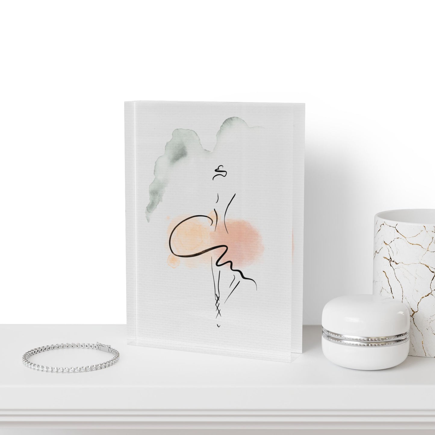 Art print of a stylized face with abstract elements on a white surface, next to a bracelet and a small container.