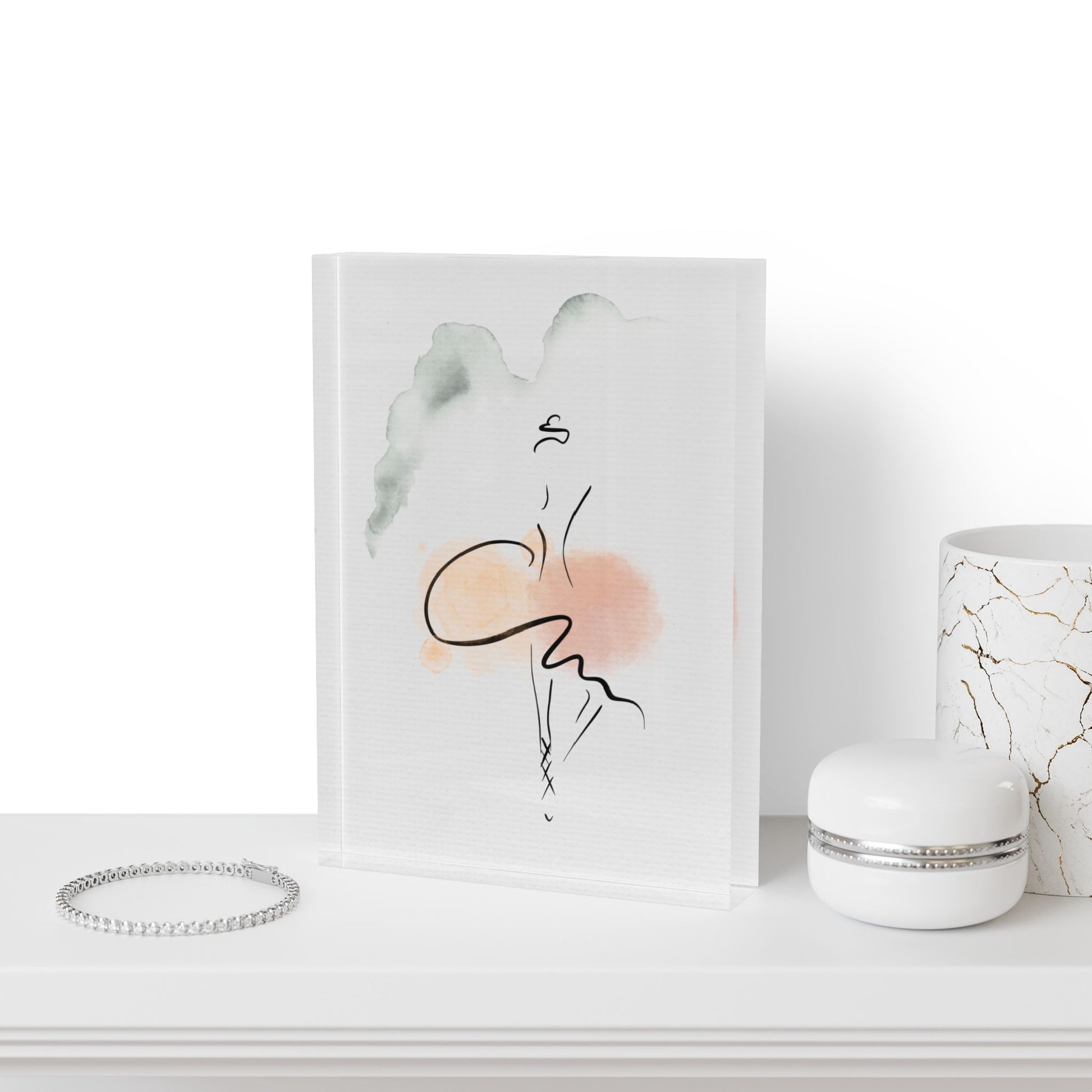 Art print of a stylized face with abstract elements on a white surface, next to a bracelet and a small container.